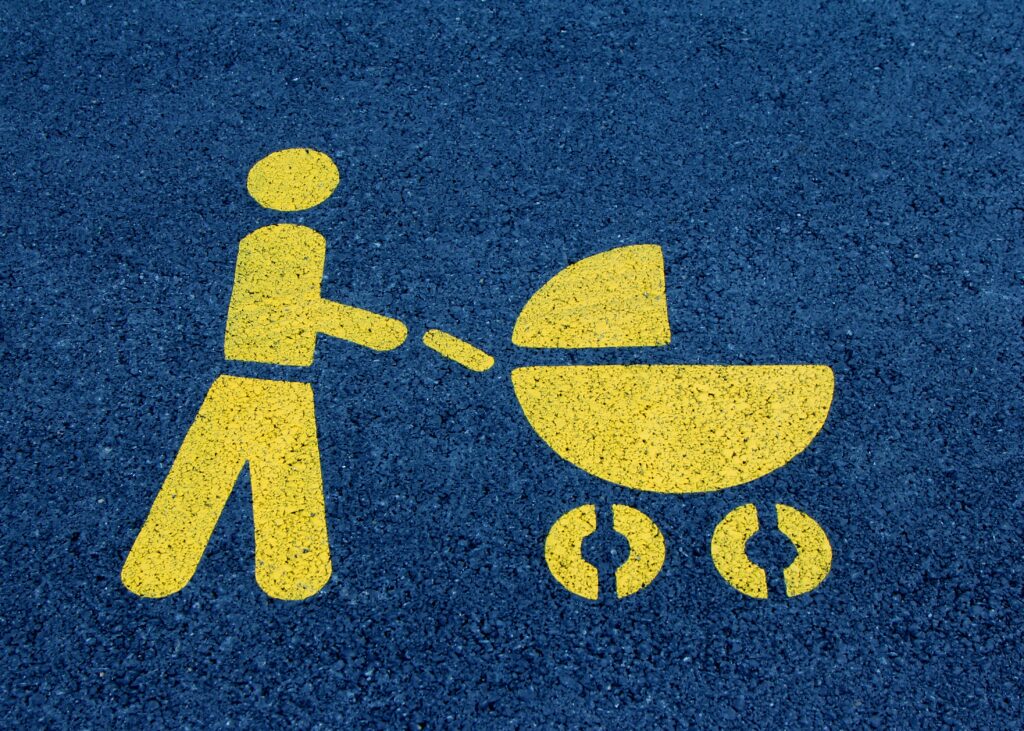 Yellow painting on tarmac of a person pushing a buggy, often use to identify a parent and child parking space
