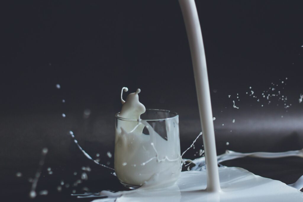 The image shows a glass of milk being poured and splashing all over the counter